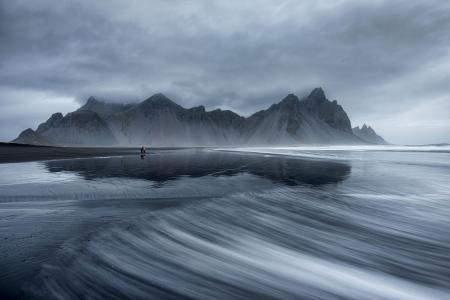 Vestrahorn et la plage de Stokksnes sont deux merveilles naturelles situées dans le sud-est de l'Islande, près de la petite ville de Höfn. Ils offrent des paysages époustouflants et sont des destinations très prisées des voyageurs et des photographes. Vestrahorn est une montagne emblématique qui se dresse majestueusement près de la côte. Elle est composée de pics pointus et de falaises abruptes, formant un paysage dramatique et impressionnant. La montagne est entourée par les eaux de l'océan Atlantique et le magnifique lac de lave de Vestrahorn. Les contrastes entre les sommets enneigés, les plages de sable noir et les eaux agitées créent une atmosphère mystique et captivante. La plage de Stokksnes est située au pied de Vestrahorn et est considérée comme l'une des plages les plus photographiées d'Islande. Elle est célèbre pour son sable noir, ses dunes de sable et ses formations rocheuses spectaculaires. Lorsque le temps est calme, le reflet des montagnes dans les mares d'eau créées par la marée basse crée des images saisissantes. La région de Vestrahorn et Stokksnes offre de nombreuses possibilités de randonnées et d'exploration. Les passionnés de photographie peuvent capturer des vues incroyables à chaque pas, en jouant avec les contrastes, la lumière et les paysages spectaculaires. Il convient de noter que Vestrahorn et la plage de Stokksnes se trouvent sur des terres privées, et pour y accéder, il est généralement nécessaire de payer des frais d'entrée à l'opérateur local. Cela contribue à la préservation et à la conservation de ces magnifiques sites naturels.